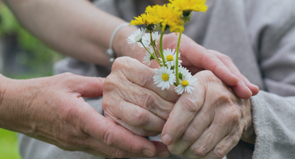 junge Person hilft einer Seniorin Blumen zu halten