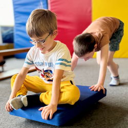 Kind sitzt auf Rollbrett und wird von anderem Kind geschoben