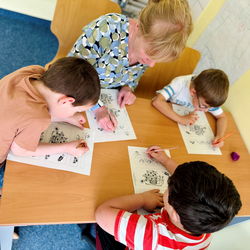 Kinder sitzen an Tisch und malen Bilder aus