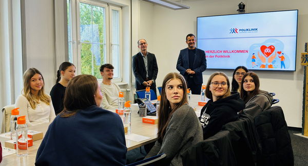 neue Auszubildende sitzen an Tisch, Geschäftsführung steht dahinter