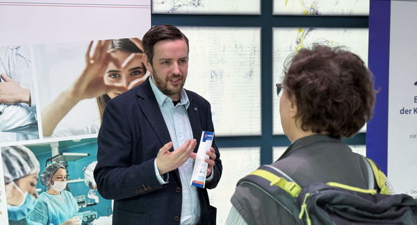 zwei Personen unterhalten sich vor Poliklinik Aufsteller