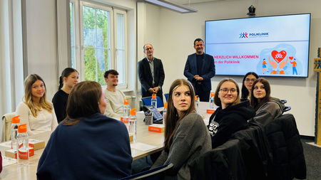 neue Auszubildende sitzen an Tisch, Geschäftsführung steht dahinter