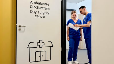 Zwei Mitarbeiter stehen im Eingang zum Ambulanten OP-Zentrum und sprechen über Dokument
