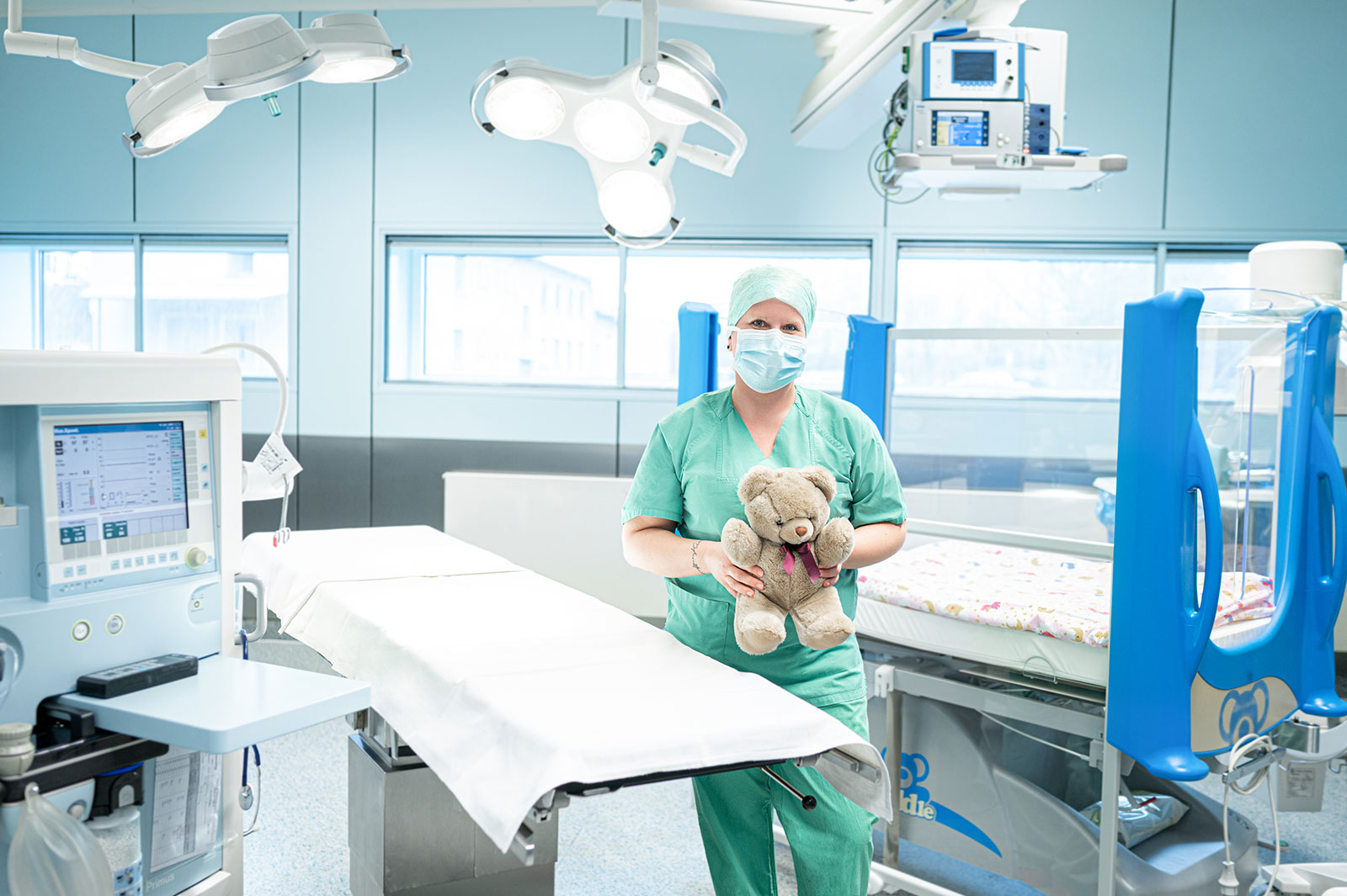 Pflegekraft steht im Aufwachraum und hält ein Kuscheltier in der Hand